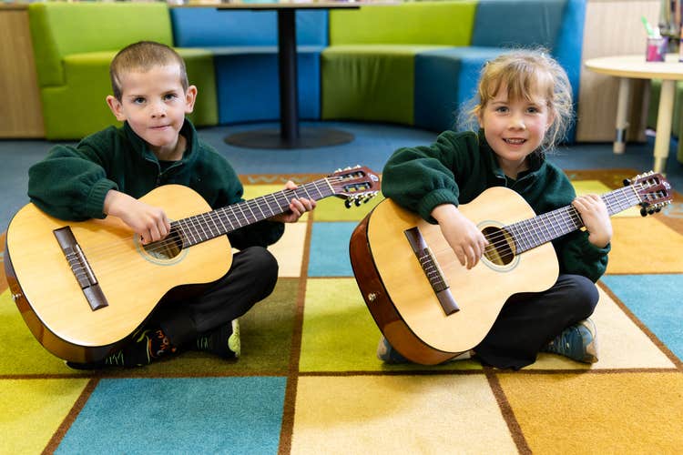 2 students playing guitar sitting on mat
