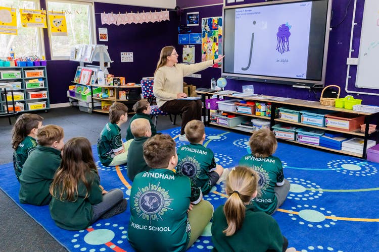 Students sitting on the mat looking at board listening to the teacher