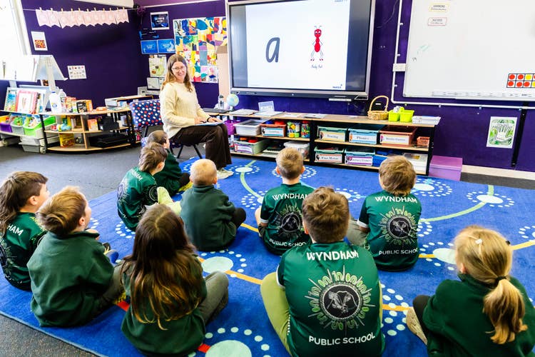 students sitting on map listening to the teacher who is explaining what is on the board